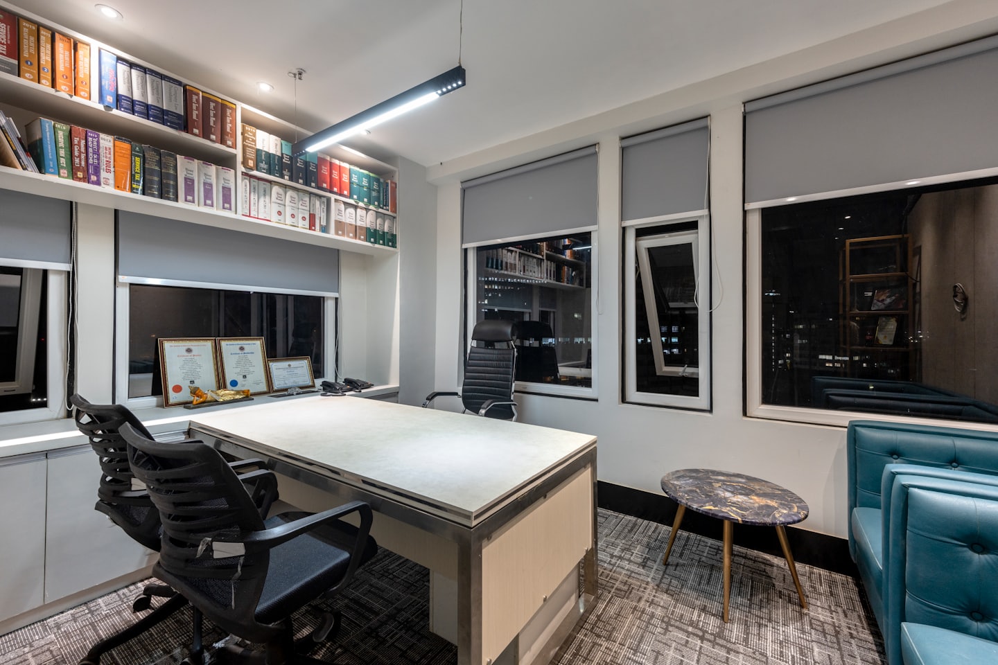 Pencerelerin yanında kitaplıklar ve masa sandalyeleri bulunan modern ofis.